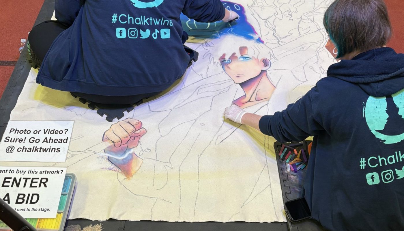 Two people do a chalk drawing on the floor at an anime convention