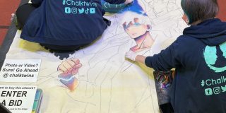 Two people do a chalk drawing on the floor at an anime convention