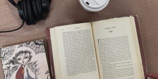 Book on table with headphones and disposable coffee cup