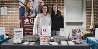 Two women stand behind GPO table